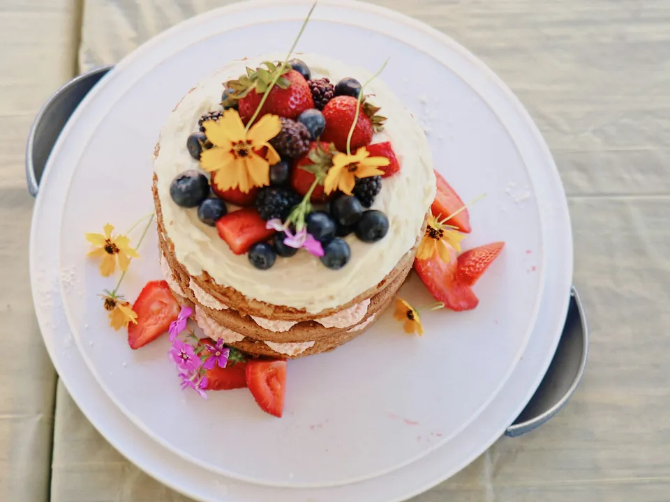 Ein Naked Cake mit Beeren und essbaren Blüten auf einem Tortenteller